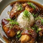 Caramelised Soy Chicken in Garlic Ginger Broth with Rice 5 Soy-glazed chicken over white rice in bowl, topped with sesame seeds and scallions.